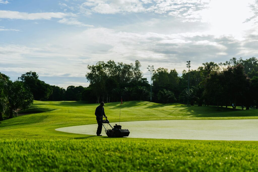 pexels-photo-27309420-27309420 Groundskeeper mowing the green on a golf course during a sunny day, showcasing lush landscapes and maintenance.